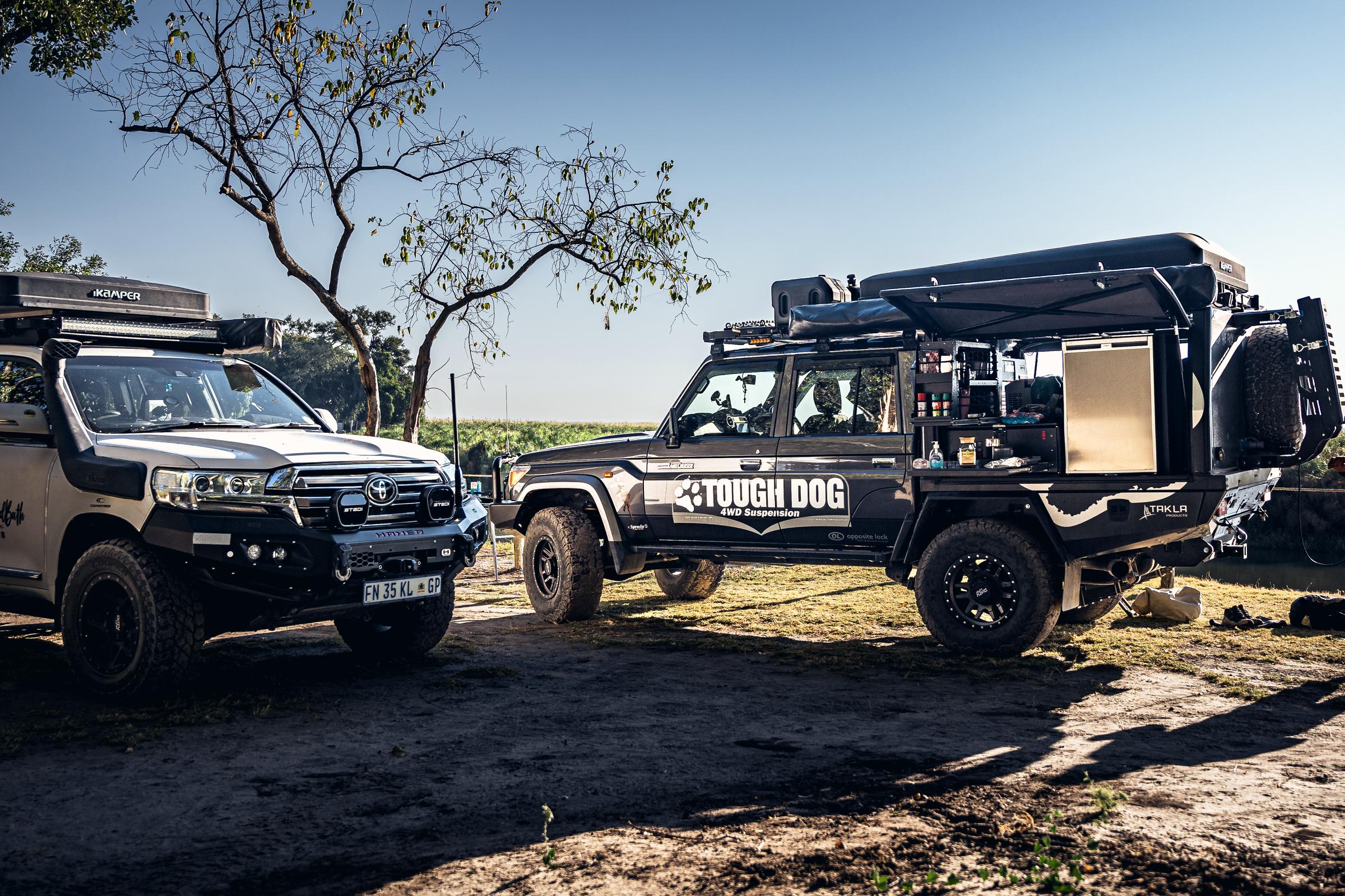 Two built-up Land Cruisers at camp, the nearer one with its canopy side door open.
