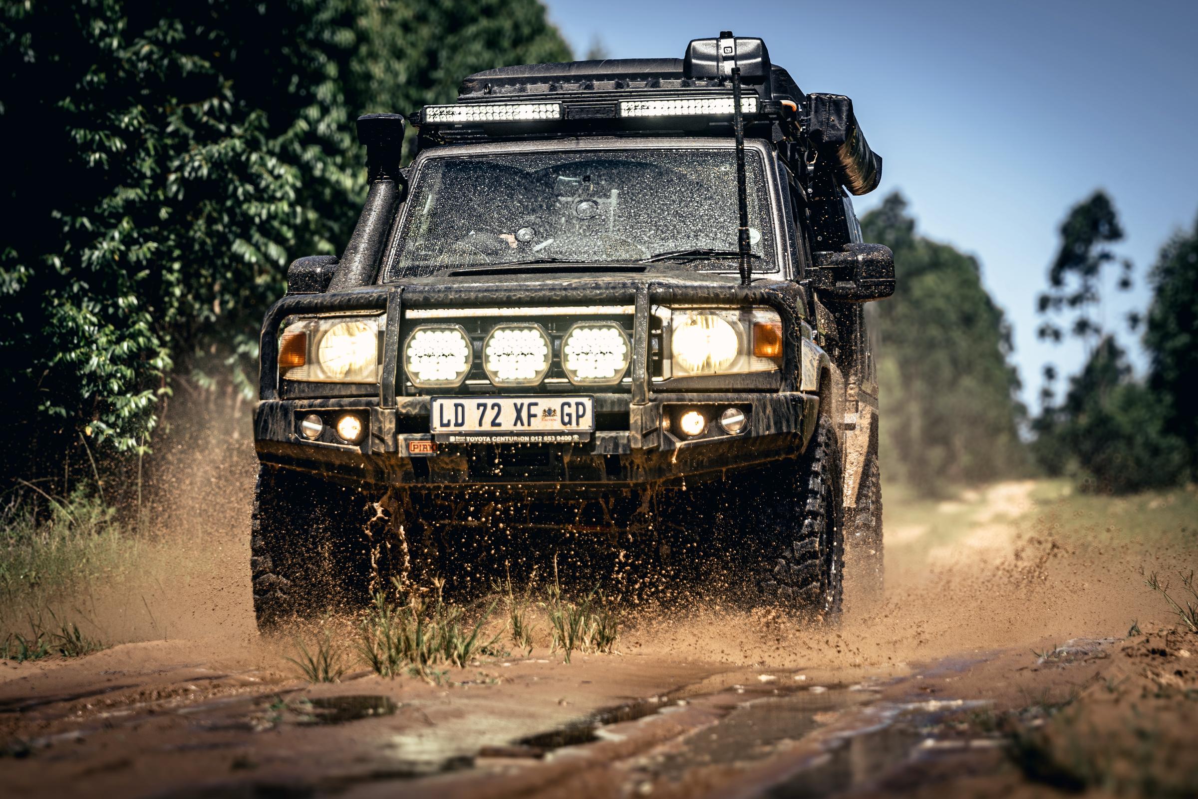 A Land Cruiser 79 driving through dust with three round LED driving lights lit on the bull bar and a light bar lit on the roof.