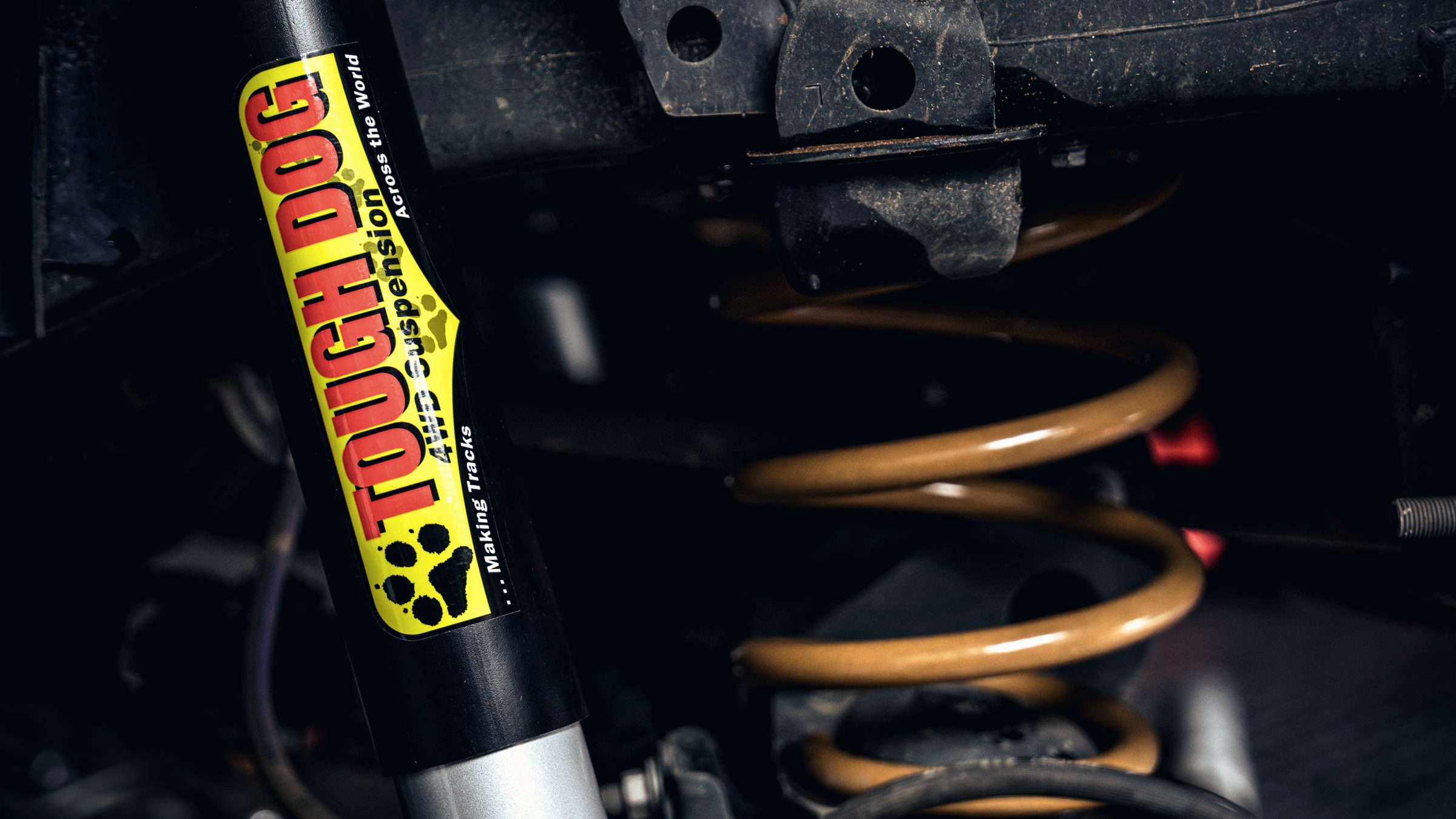 A Tough Dog shock absorber and coil spring fitted under a vehicle, seen from below.